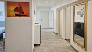 Un pasillo de hotel con un cuadro de un velero, un mostrador de recepción blanco y un espejo grande a la derecha.