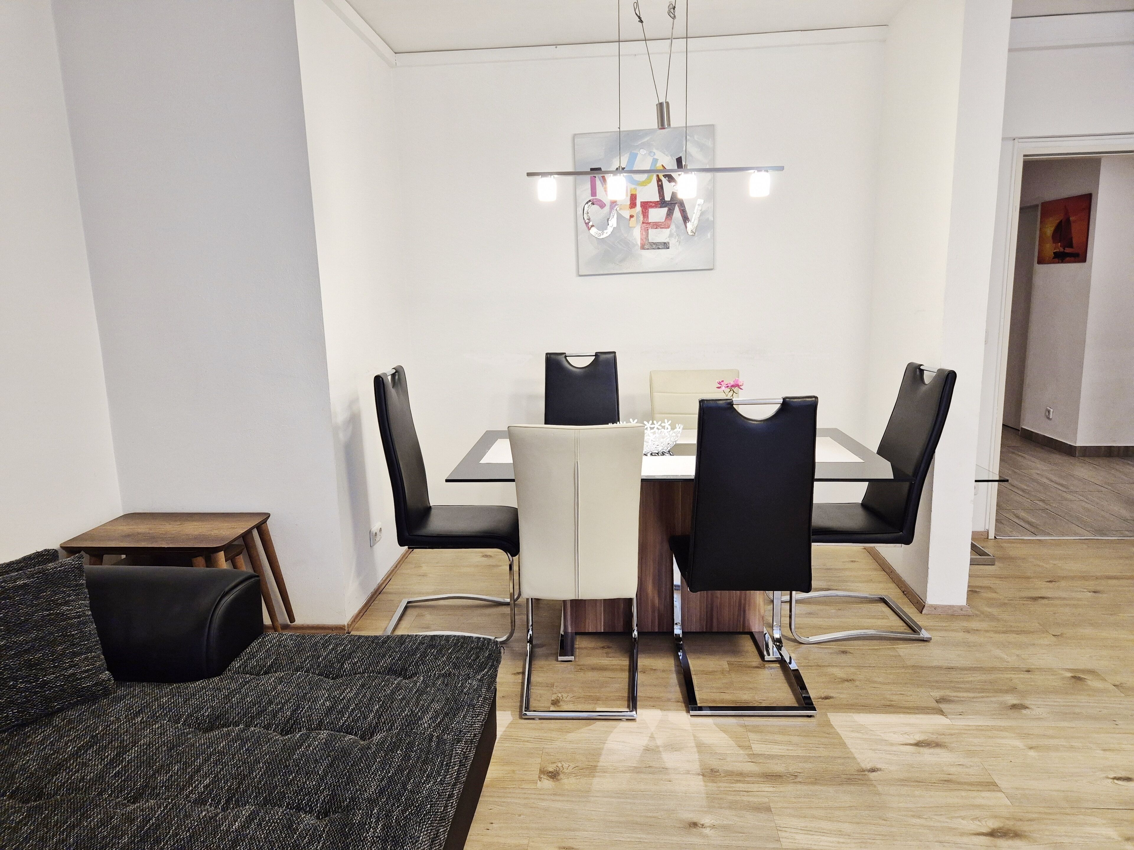 A modern dining area with a glass table, black and white chairs, and a hanging light fixture.