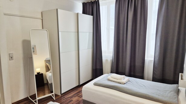 Habitación de hotel con cama, armario, espejo y ventana con cortinas.