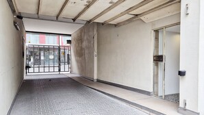 Un pasillo con suelo de baldosas, una puerta metálica y una puerta que da a una habitación donde se ve un enchufe.
