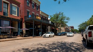 A street with buildings, outdoor seating, and parked cars.