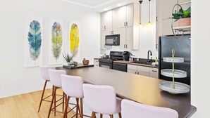 A modern kitchen with a central island, bar stools, a two-tiered serving tray, and decorative feather wall art.