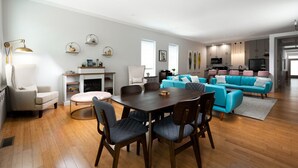 A modern living room with a dining area, a fireplace, and a kitchen in the background.