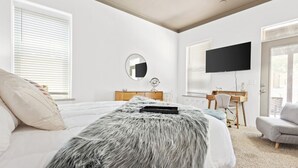 A bedroom with a bed, a desk, a chair, a TV, and a window.