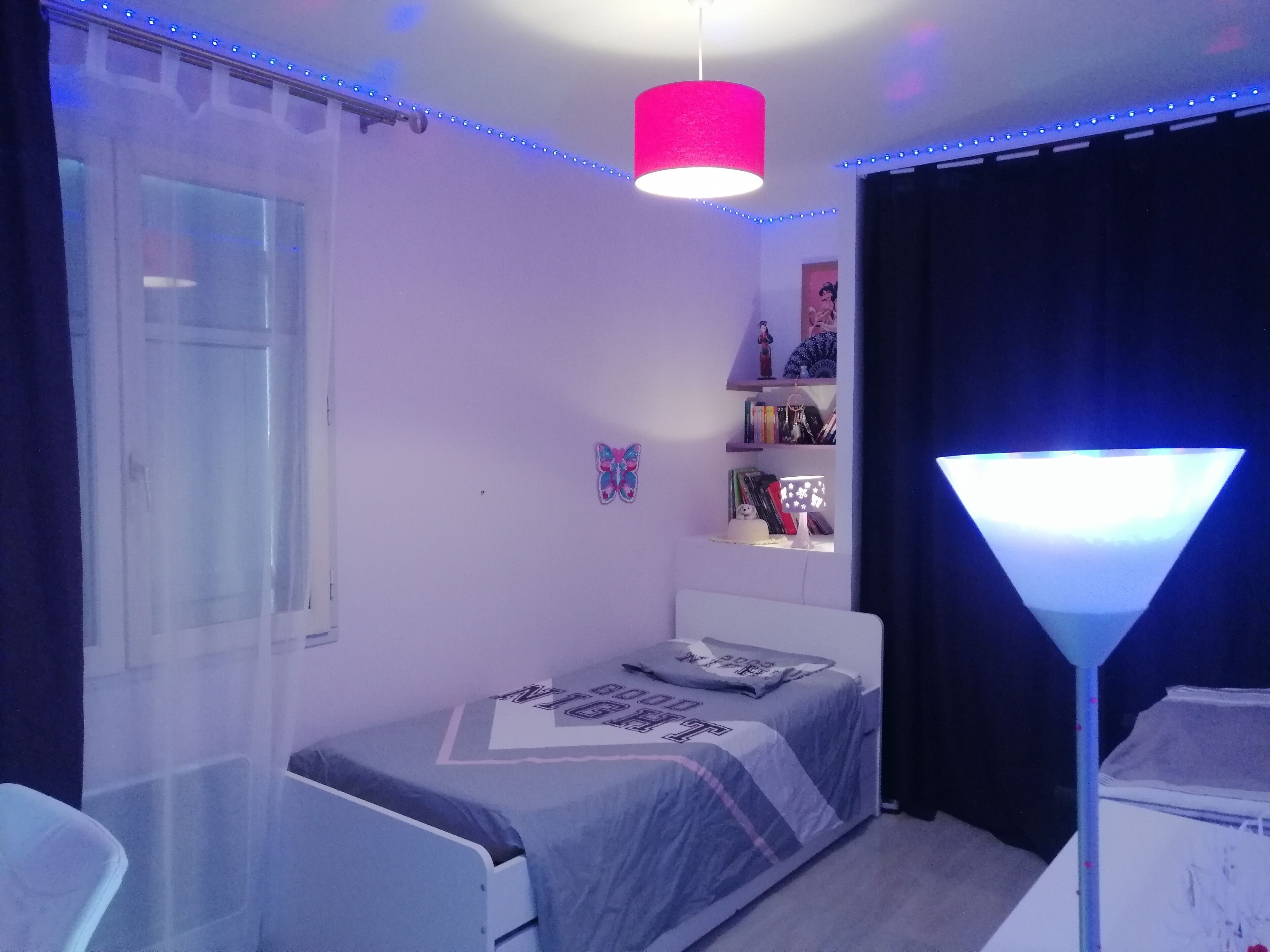 Une chambre à coucher comprenant un lit, un bureau, une lampe et une étagère avec des livres et des objets décoratifs.