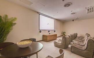 Una sala conferenze con schermo proiettore, una scrivania in legno, poltrone a sacco e un tavolo da pranzo con un recipiente pieno di popcorn.