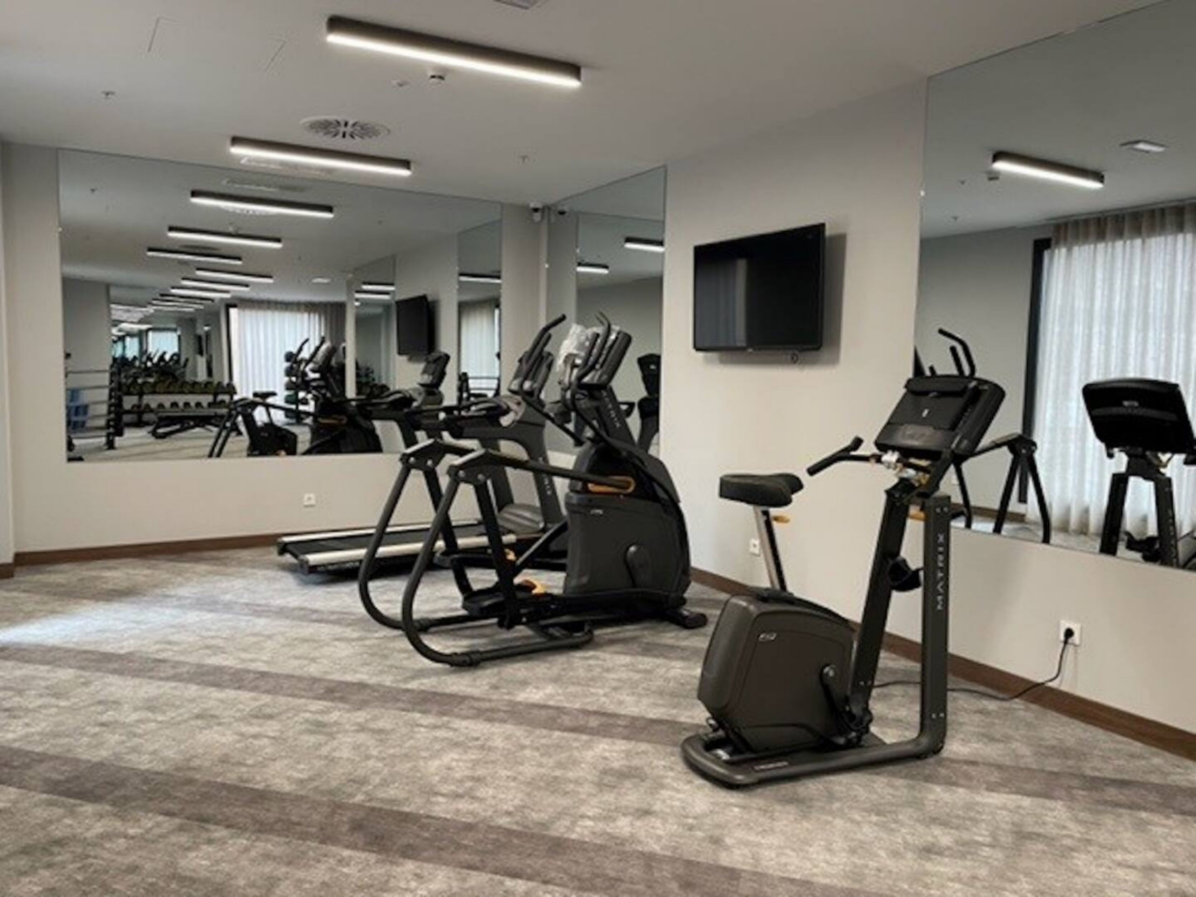Ein Fitnessraum mit Laufbändern, Ergometer und einer Spiegelwand.