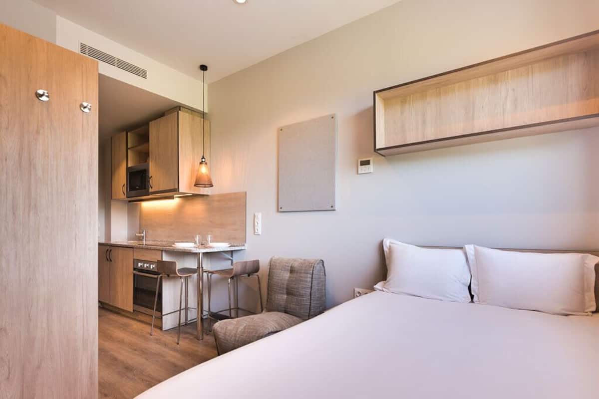 Une chambre d’hôtel comprenant un lit, un bureau avec une chaise, un four à micro-ondes et une petite kitchenette.