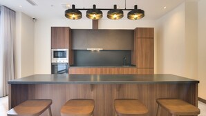 Une cuisine moderne dotée d’un îlot central, de tabourets de bar, d’appareils électroménagers intégrés et de luminaires suspendus.