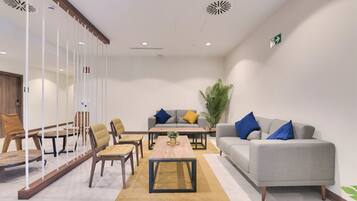 A modern, well-lit room with a grey sofa, two armchairs, a coffee table, and a large potted plant.
