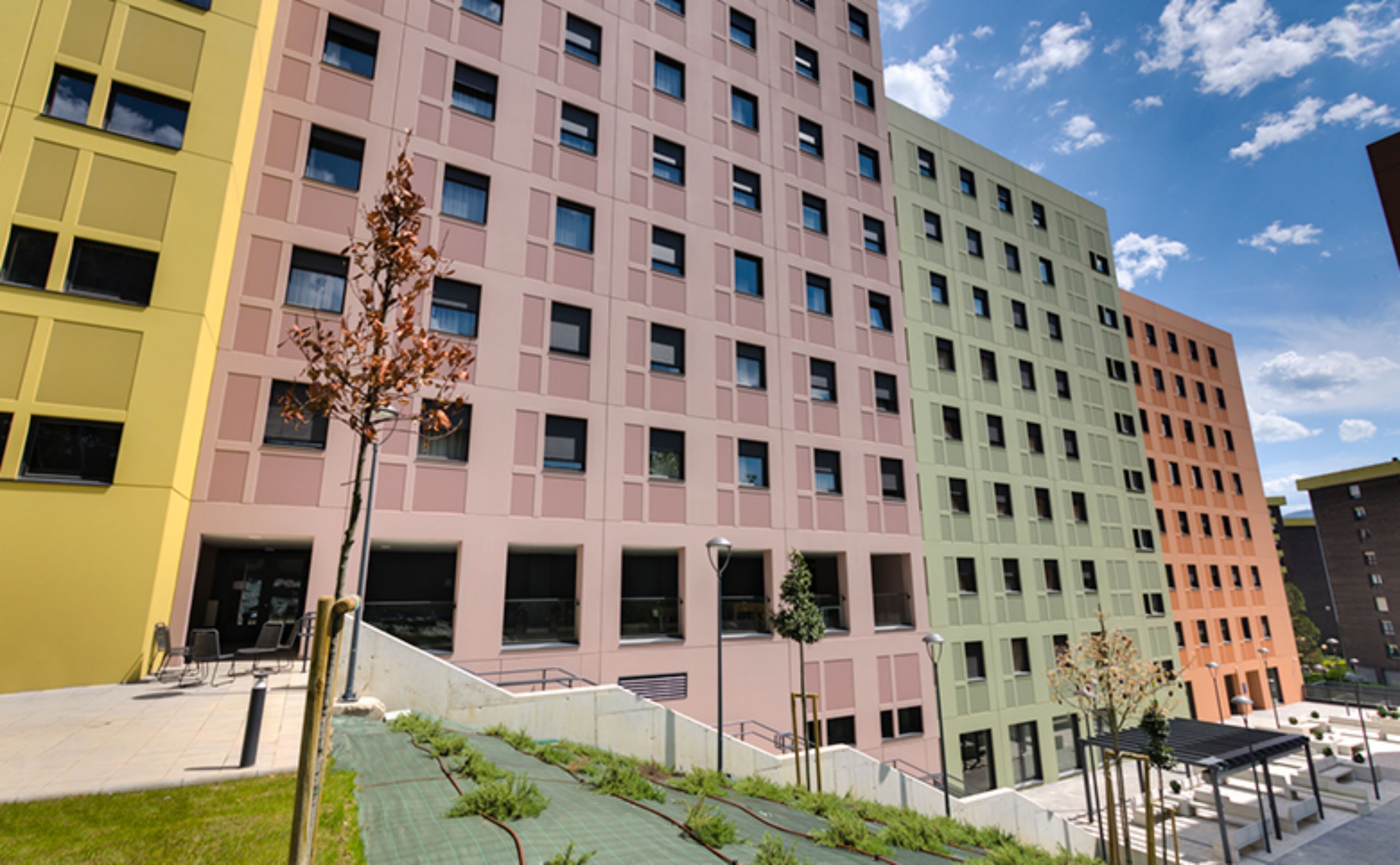 Edifici d'aquestes alçades amb un disseny arquitectònic modern, amb una sèrie de balcons i un jardí verd a la teulada.