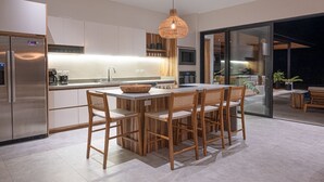 A modern kitchen with a central island, stainless steel appliances, and a dining area with wooden chairs. - Casa Zuri Luxury Villa + Guest House & Beach Club (Tamarindo)