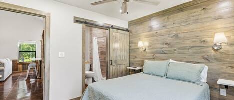 Un dormitorio con cama, ventilador de techo, paneles de madera y una ventana.