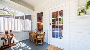 A covered porch with a table and chairs, a door leading to a room, and a window with blinds.