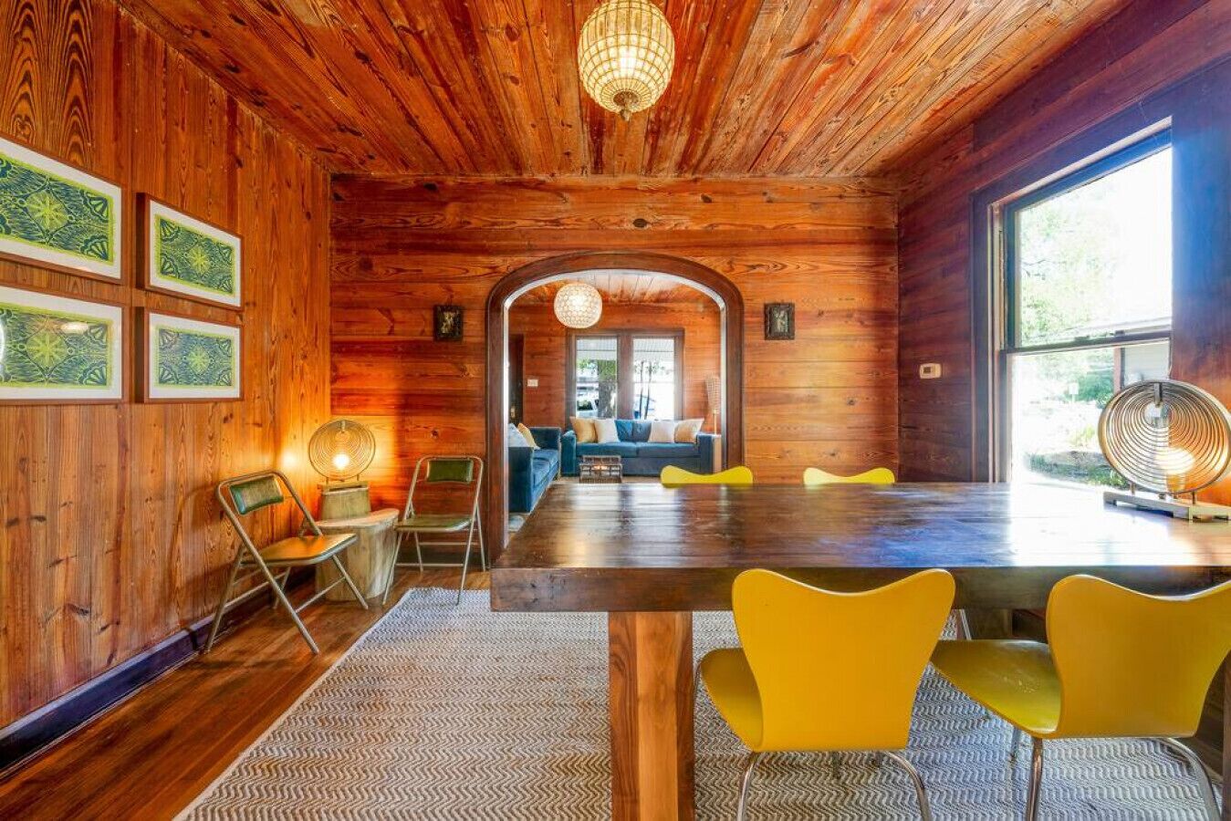 A wooden interior with a dining area, yellow chairs, and a large window.