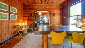 A wooden interior with a dining area, yellow chairs, and a large window.