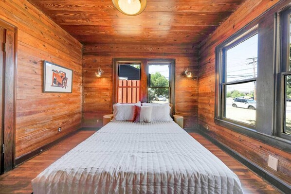 A wooden cabin bedroom with a bed, a framed picture, and a window with a view of the outside.