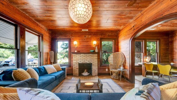 A cozy living room with a fireplace, wooden walls, and large windows.