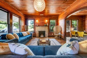 A cozy living room with a fireplace, wooden walls, and large windows. - Adorable Historic Home, Super Close to UT, Moody Center, and Downtown (Austin)