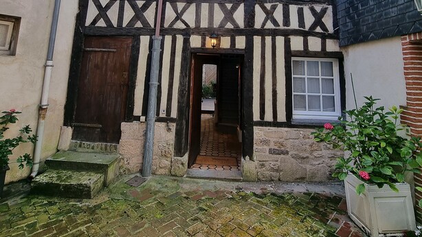 Une maison traditionnelle à colombages, dotée d’une façade en bois sombre et d’un enduit blanc.