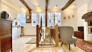 Une pièce spacieuse avec un escalier en bois, un fauteuil gris et un téléviseur posé sur une commode en bois.