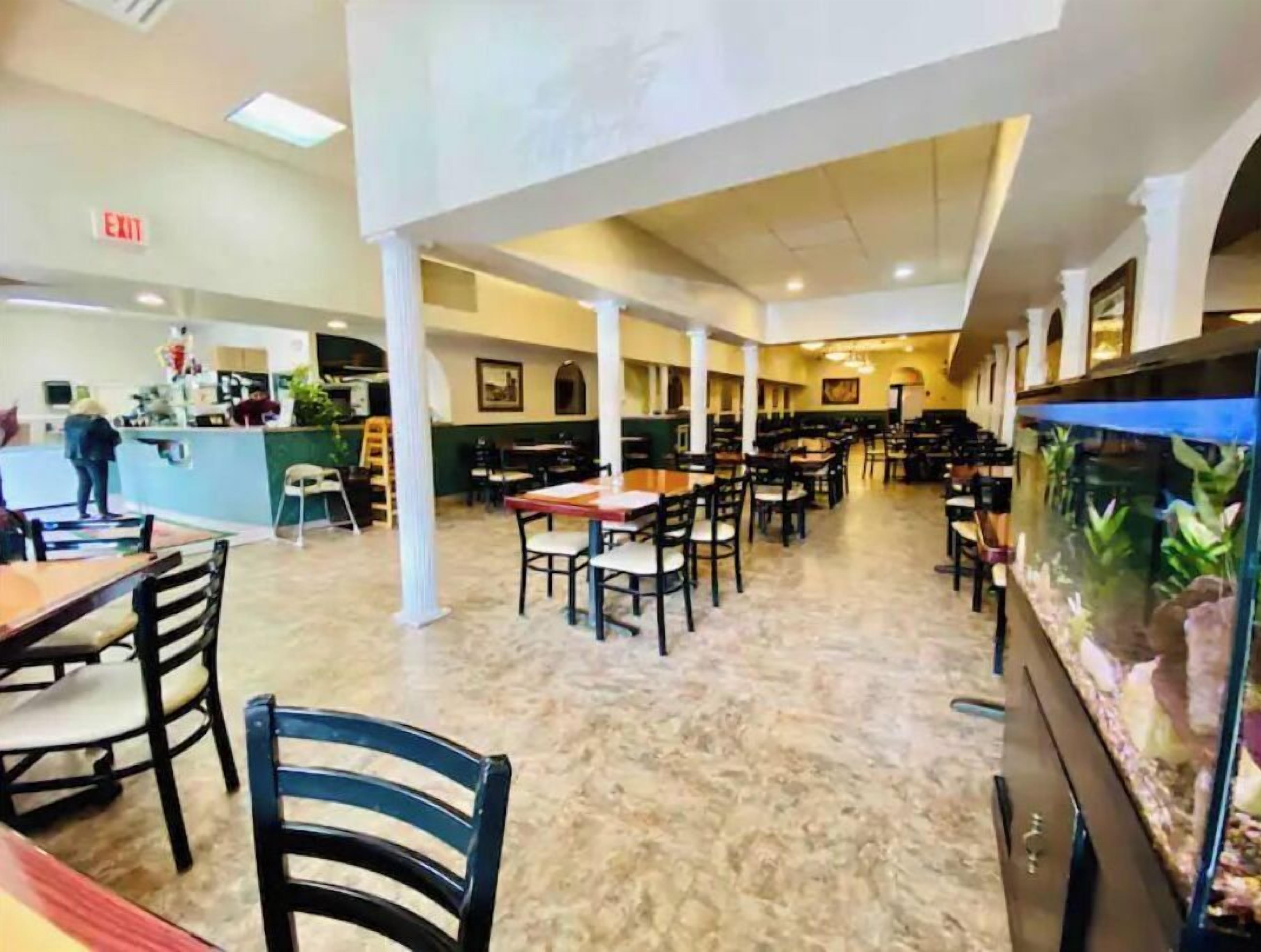A spacious restaurant with high ceilings, multiple tables and chairs, and a large aquarium.