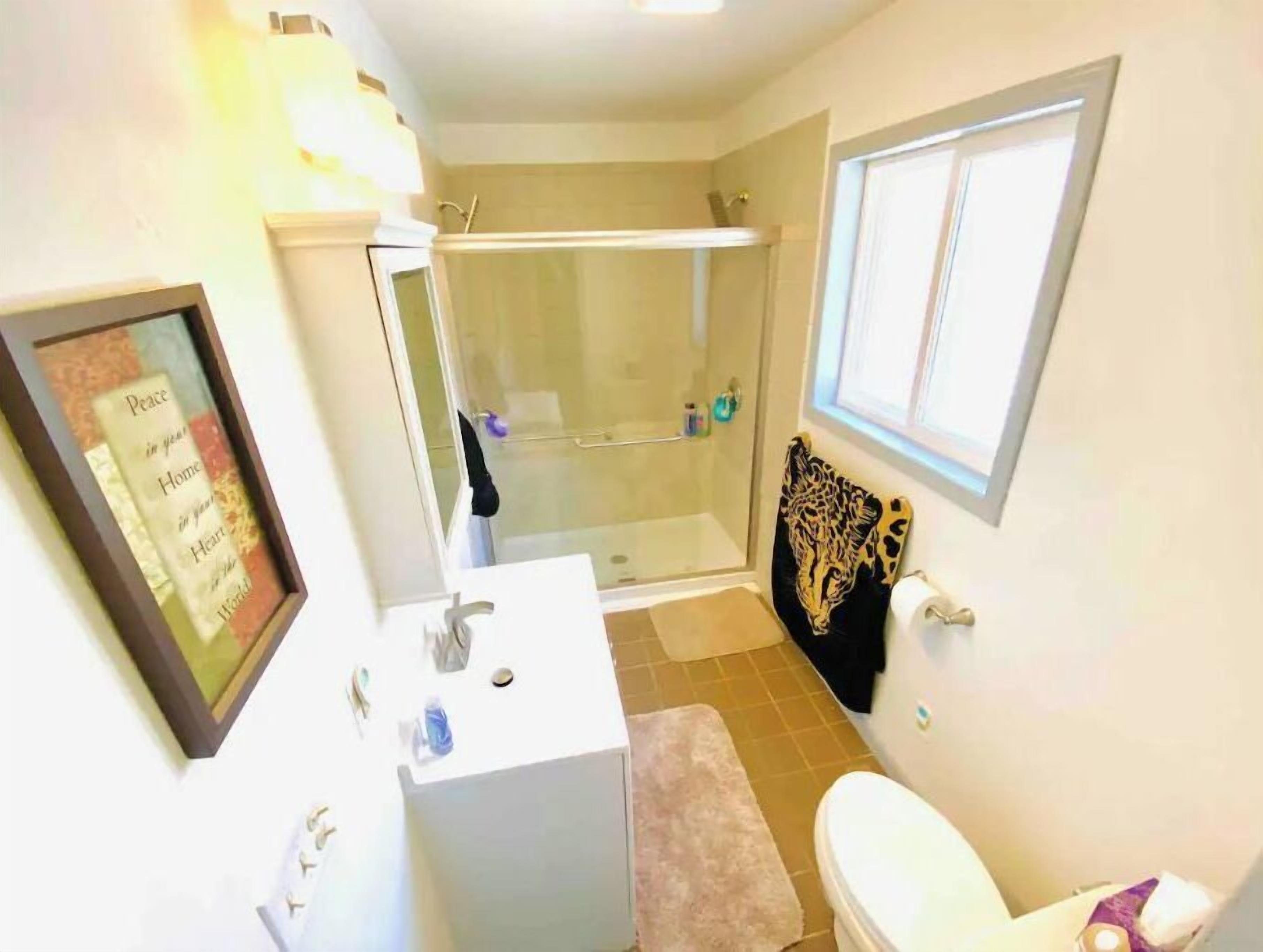 Une salle de bain équipée d’une douche, de toilettes, d’un lavabo et d’une citation inspirante encadrée au mur.