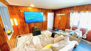Un salon chaleureux avec une grande télévision, des murs en bois, un canapé et une petite table d’appoint.