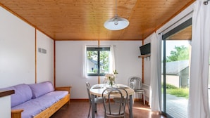 Una habitación acogedora con techo de madera, un sofá morado, una mesa redonda con sillas para comer y una ventana con vistas al exterior.