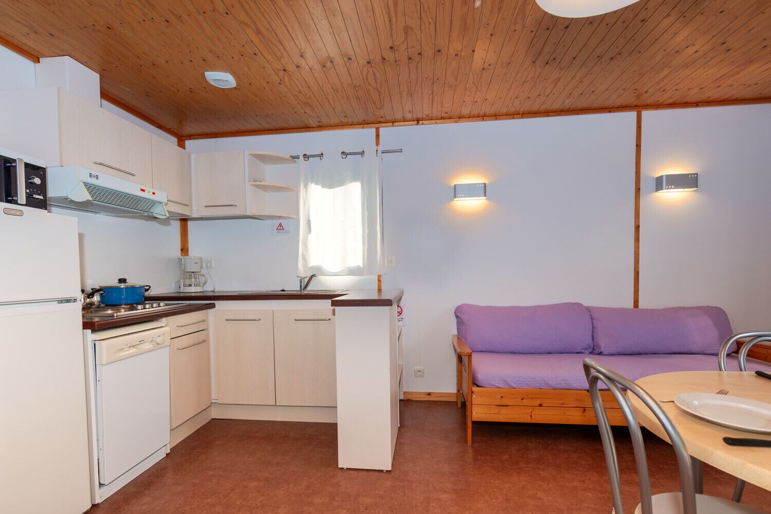 Eine kleine Wohnfläche mit einer kompakten Küche, ausgestattet mit Herd, Spüle und einem violetten Sofa.