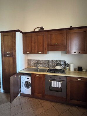 Une cuisine avec des meubles de rangement en bois, un lave-linge, une cuisinière et un évier.