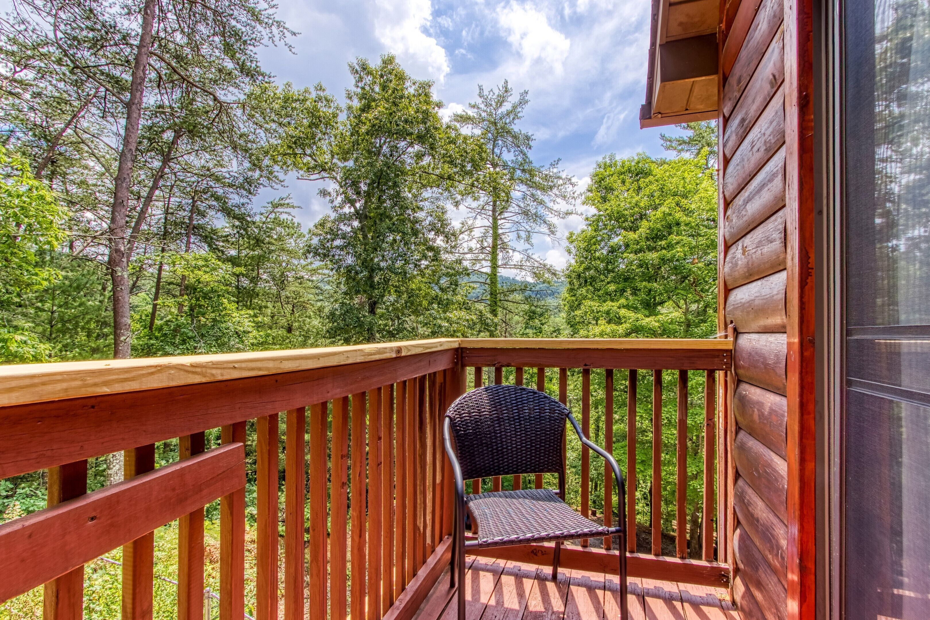 A wooden deck with a metal chair, surrounded by lush greenery and trees.