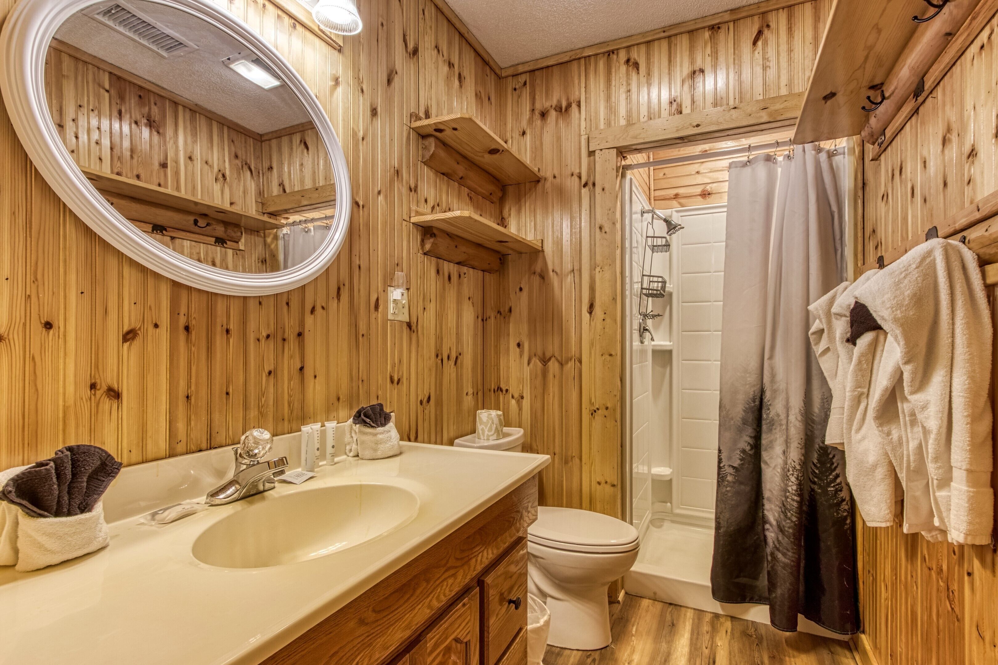 A wooden-paneled bathroom with a sink, mirror, toilet, and shower.