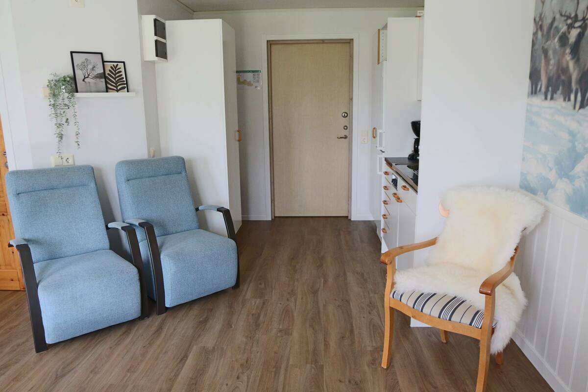A living room with two blue armchairs, a wooden chair with a fur throw, and a door leading to another room.