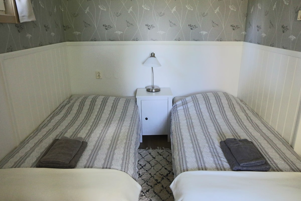 A twin room with two beds, a nightstand, a lamp, and a patterned wall.
