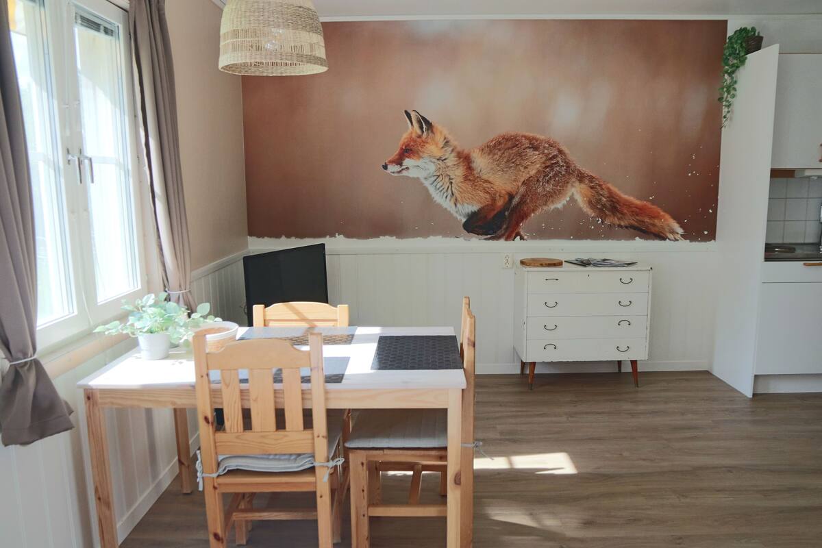 A dining area with a wooden table and chairs, a white cabinet with drawers, and a large wall mural of a fox.