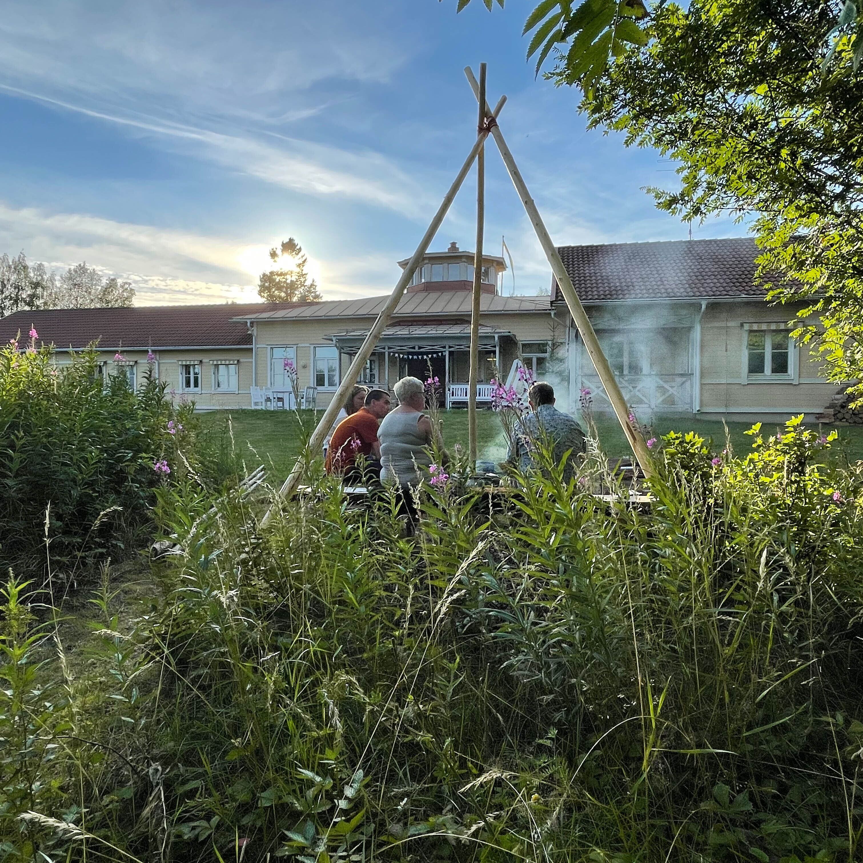 A group of people gathered around a wooden structure in a garden area with a building in the background.
