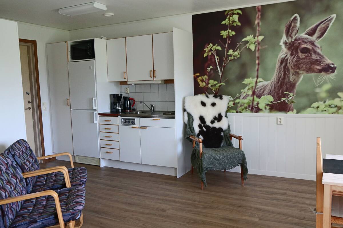 A modern living room with a sofa, a chair with a unique design, and a kitchen in the background.