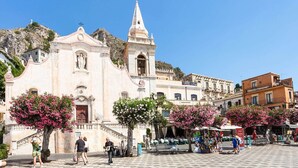 Una iglesia histórica con un campanario, rodeada por una plaza adoquinada con tiendas y cafés.