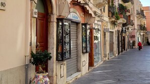 Una calle con edificios, una bandera y una tienda con persianas cerradas.