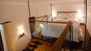 Quarto com cama, mesa de cabeceira, luminária na parede e janela com cortina.