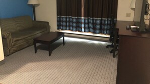 A living room with a sofa, a coffee table, a TV, and a window with curtains. - AmeriVu Inn & Suites (Eau Claire)