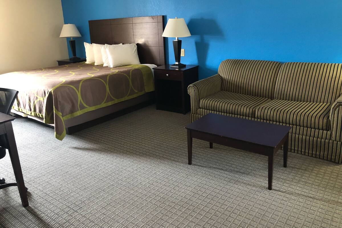 A hotel room with a bed, two bedside lamps, a striped sofa, and a small table.