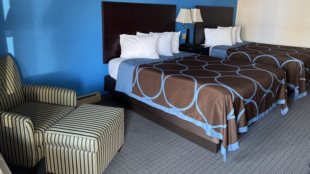 A hotel room with a large bed, a striped armchair, and a nightstand with a lamp. - AmeriVu Inn & Suites (Eau Claire)