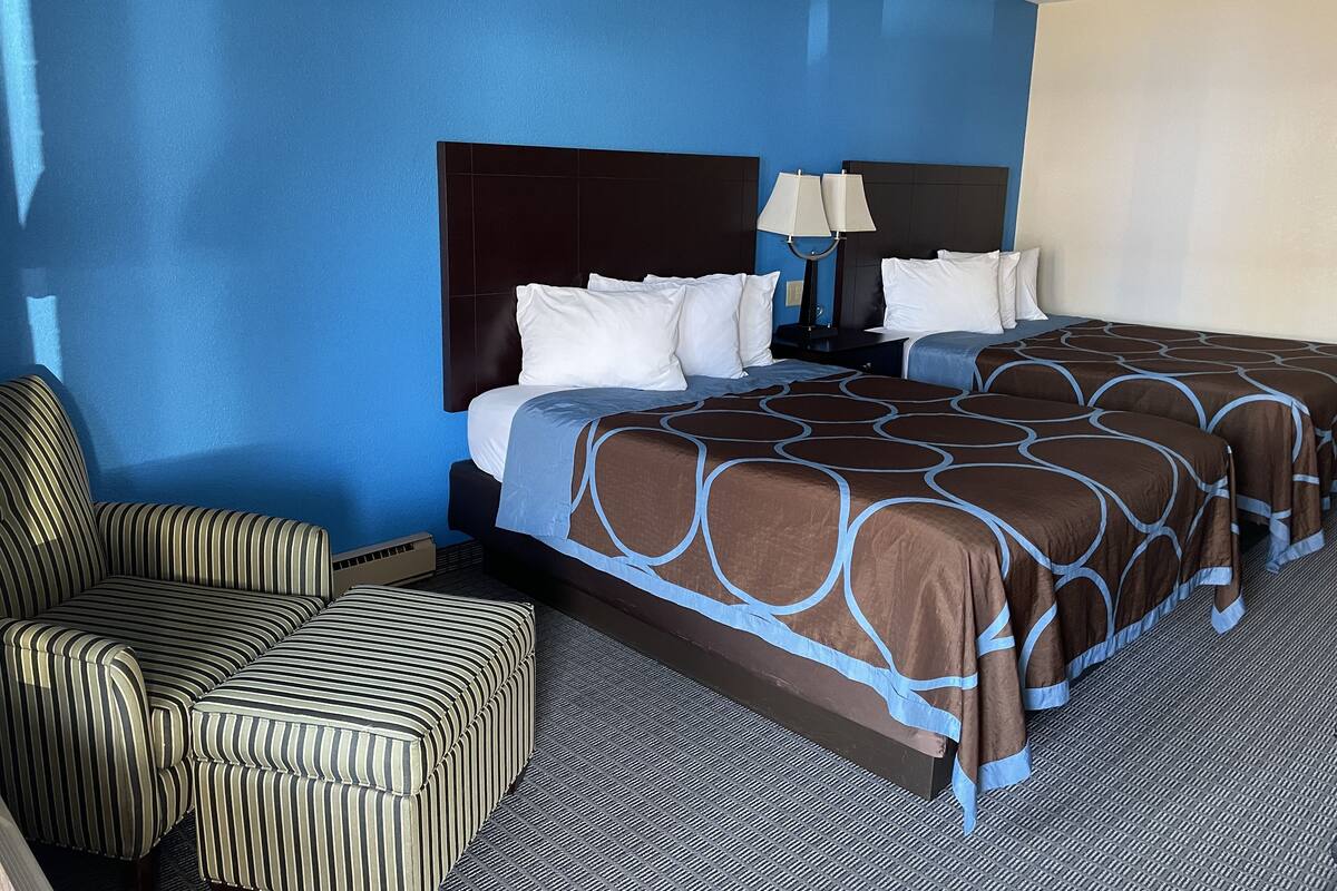 A hotel room with a large bed, a striped armchair, and a nightstand with a lamp.