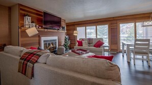 Ein gemütliches Wohnzimmer mit Kamin, einem an der Wand montierten Fernseher und einem Weihnachtsbaum.