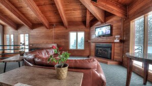 Ein Holzblockhaus-Innenraum mit einer Ledersofa, einem Kamin, einem Fernseher und einem Esstisch.