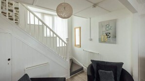 A staircase with white railings, a textured ceiling light, a framed artwork, and a black armchair. - Cosy Welsh Cottage in St Davids Centre with Garden (St Davids)