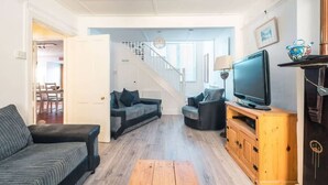 A modern living room with a sofa, a television on a wooden stand, and a staircase leading to another room. - Cosy Welsh Cottage in St Davids Centre with Garden (St Davids)
