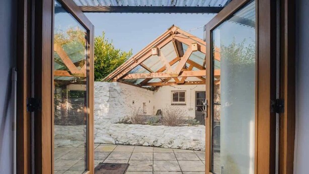 A view through a glass door into a room with a stone wall, wooden beams, and a tiled floor. - Cosy Welsh Cottage in St Davids Centre with Garden (St Davids)